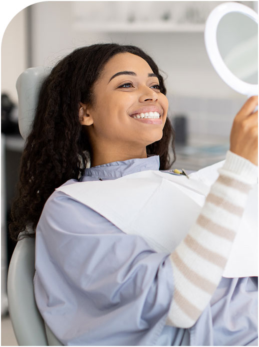Stock image of a smiling patient checking her teeth in mirror